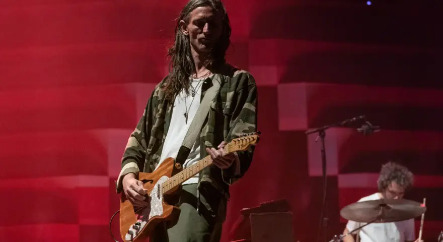 Nick Valensi spielt Gitarre auf einer Bühne, im Hintergrund ein Schlagzeuger.