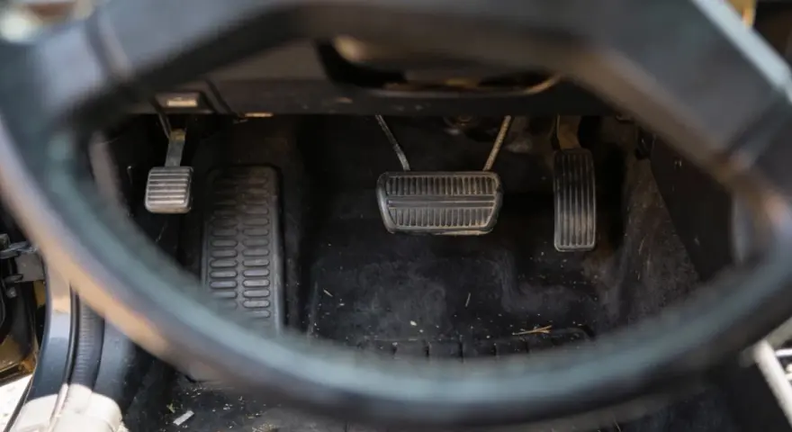 Widok na pedały samochodu. Sprzęgło, hamulec i gaz. Uważaj na jazdę na półsprzęgle, bo to męczy auto.