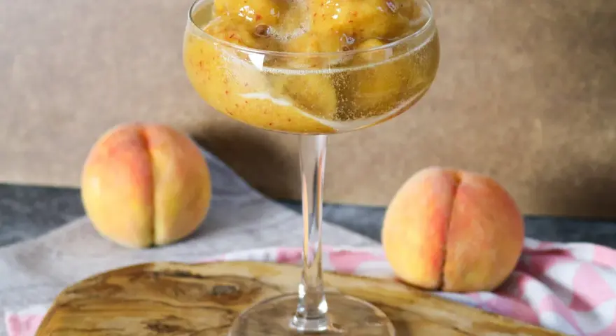 Erfrischendes Pfirsich-Prosecco-Sorbet in einem eleganten Glas, daneben reife Pfirsiche.