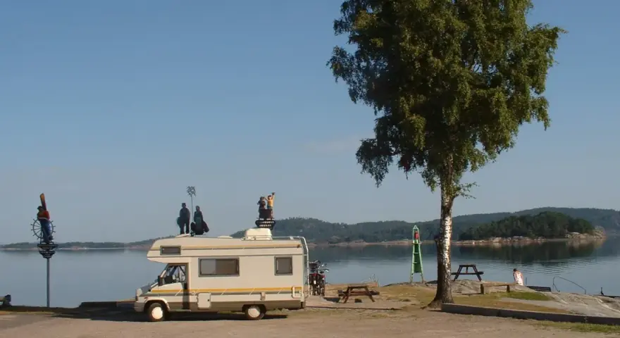 Husbil vid vattnet med figurer på taket, redo för året runt camping. En vacker plats för avkoppling.