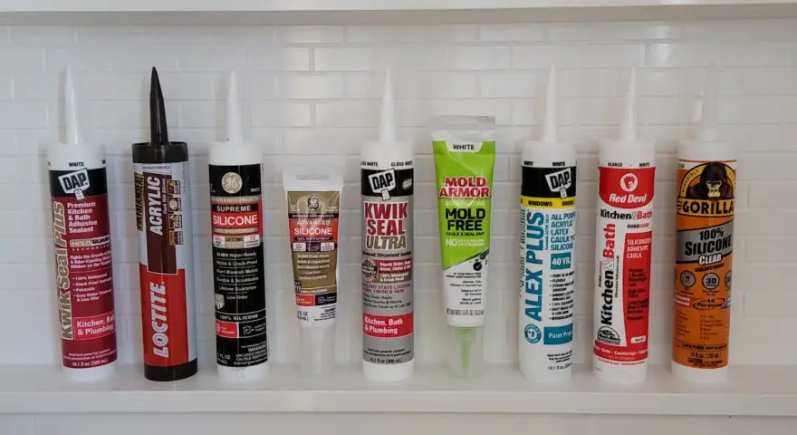 A variety of caulking tubes are lined up, ready for anyone wanting to learn how to caulk a shower. Brands include DAP, Loctite, GE, Mold Armor, Alex Plus, Red Devil, and Gorilla.