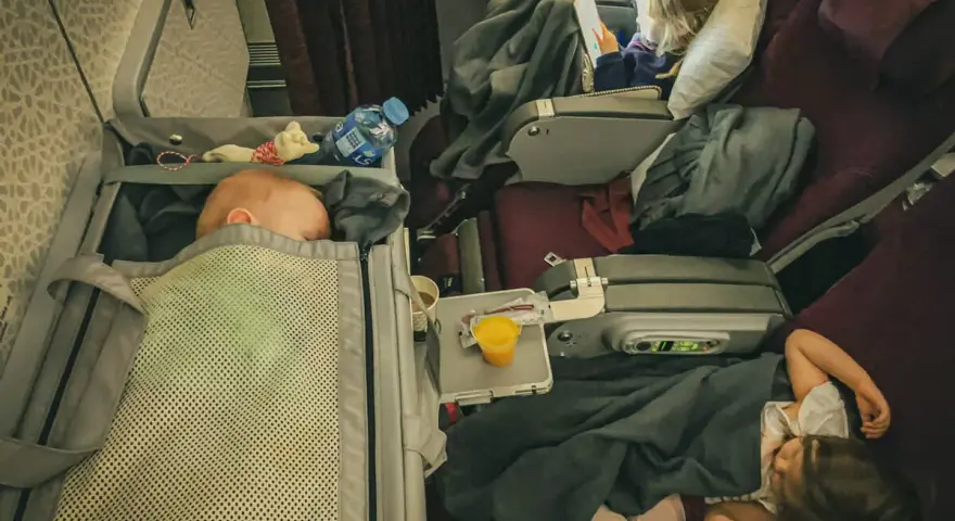 Lot z niemowlakiem i śpiącymi dziećmi w samolocie. Maluch odpoczywa w gondoli, starszaki pod kołderkami.