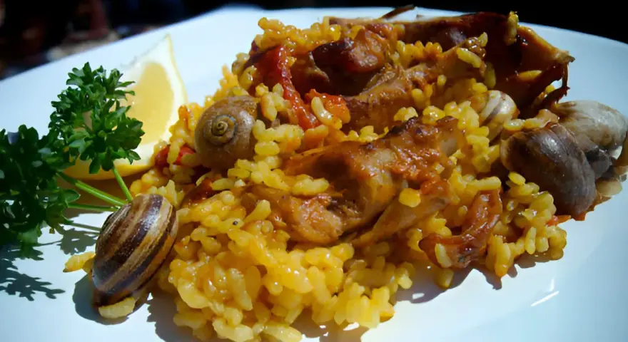 Arroz con conejo, un plato tradicional con trozos de carne dorada, arroz amarillo y caracoles, adornado con perejil y limón.