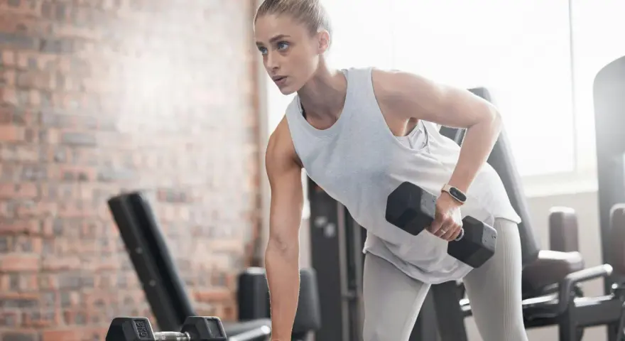 Kvinna tränar med hantlar på gym, fokuserad på att bygga muskler och gå upp i vikt.
