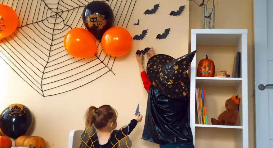 Dzieci tworzą **dekoracje halloween diy**: wieszają nietoperze na ścianie, obok pajęczyny i balonów.