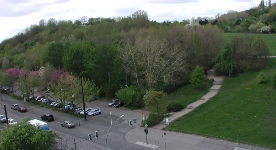 Grüne Hügel und Bäume im Volkspark Prenzlauer Berg. Autos parken am Straßenrand, eine Treppe führt einen Hang hinauf.