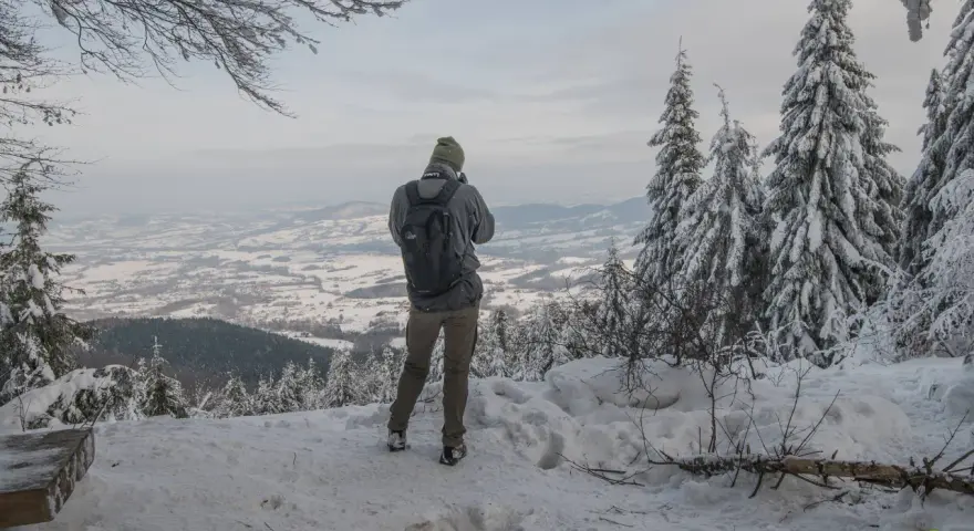 Turysta podziwia zimowy krajobraz z Lubomira. Najkrótszy szlak prowadzi przez ośnieżone drzewa do punktu widokowego.