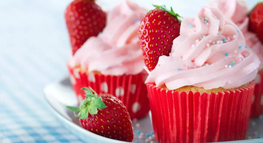 Erdbeer cupcakes mit rosa Zuckerguss und frischen Erdbeeren, verziert mit bunten Streuseln.