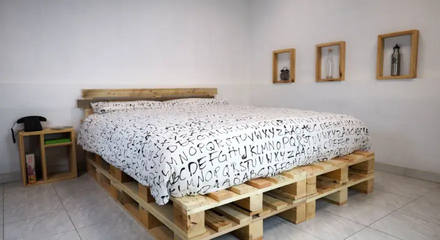 Un letto fai da te economico realizzato con pallet di legno, con un copriletto bianco e nero a tema alfabetico.