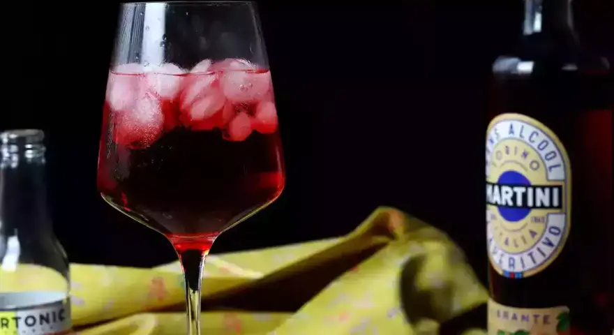 Orzeźwiający martini z tonikiem, z lodem i owocowym akcentem, obok butelki toniku i butelki Martini.