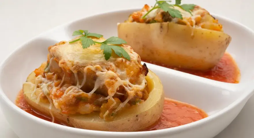 Patatas rellenas de carne de la abuela, gratinadas con queso y perejil, servidas con salsa de tomate.