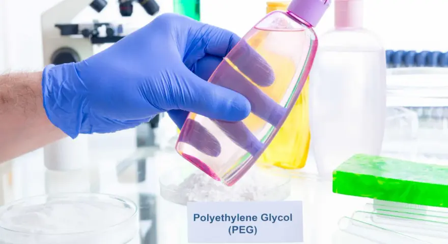 Ręka w niebieskiej rękawiczce trzyma buteleczkę z różowym płynem, w tle laboratorium i kosmetyki.