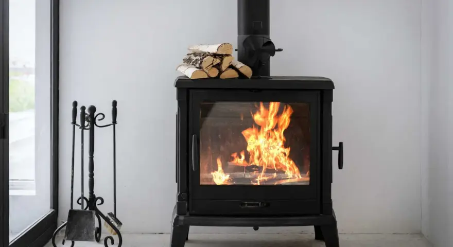Estufa de leña con fuego vivo, lista para canalizar aire y chimenea. A su lado, un atizador y escoba.