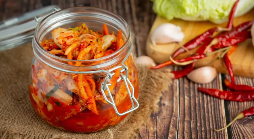 Słoik z kimchi na tle desek, z kapustą, czosnkiem i papryczkami chili.