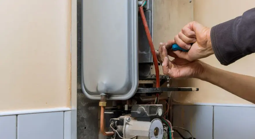 Mani che riparano uno scaldabagno a gas: il bruciatore non parte. Si vede il tecnico con un cacciavite blu.
