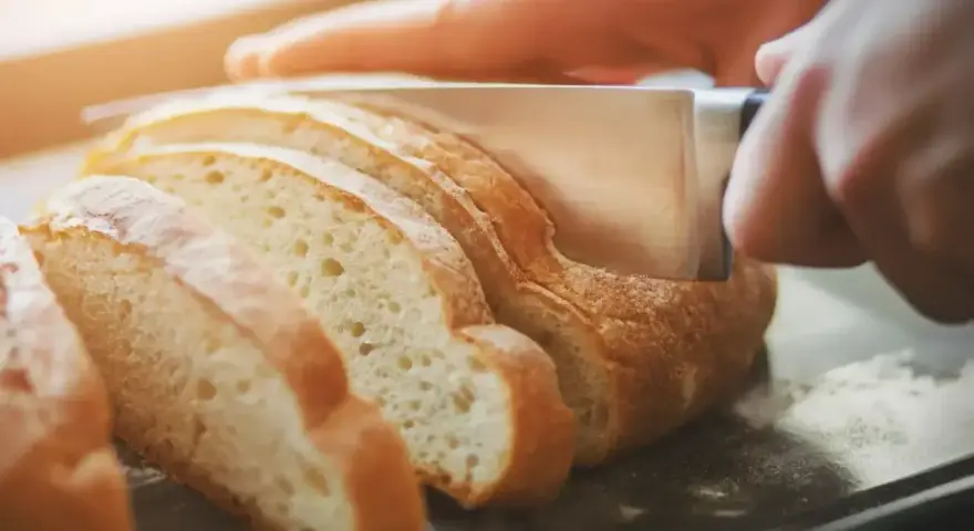 Ręce kroją świeży chleb na kromki. Dowiedz się, jak odświeżyć chleb, by był jak nowy.