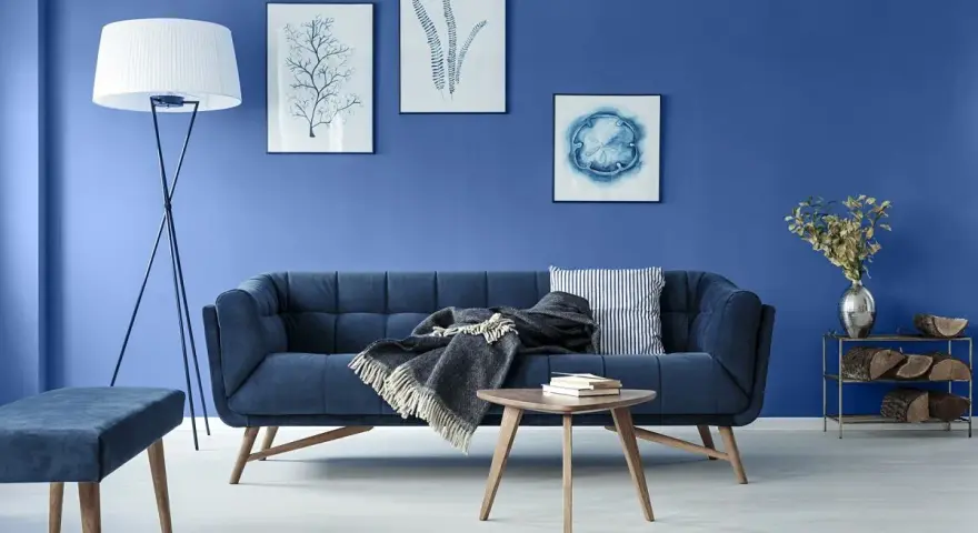 Nowoczesny salon w odcieniach koloru niebieskiego. Granatowa sofa, fotel, dywan i obrazy tworzą spójną, spokojną aranżację.