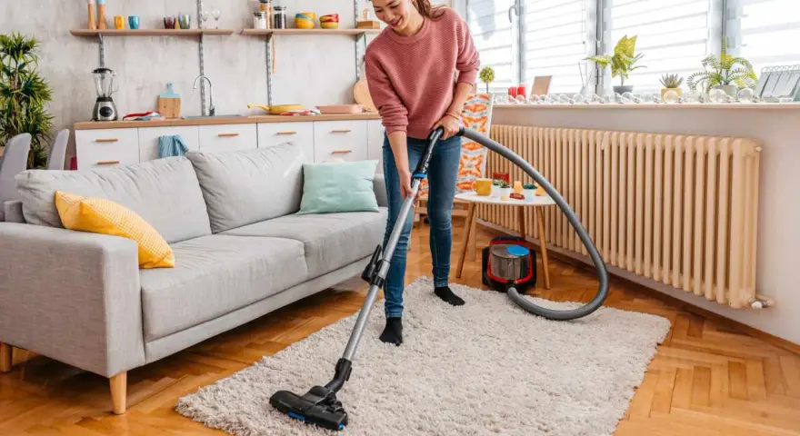 A woman vacuums a fluffy rug, demonstrating how to clean a rug for a fresh, tidy living room.