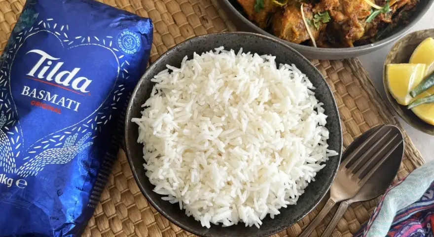 Un tazón de arroz basmati blanco y esponjoso junto a un paquete de Tilda Basmati Original.
