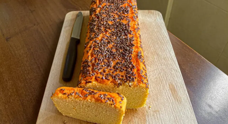 Pane di lenticchie con semi di lino, affettato su tagliere di legno, accanto a un coltello.