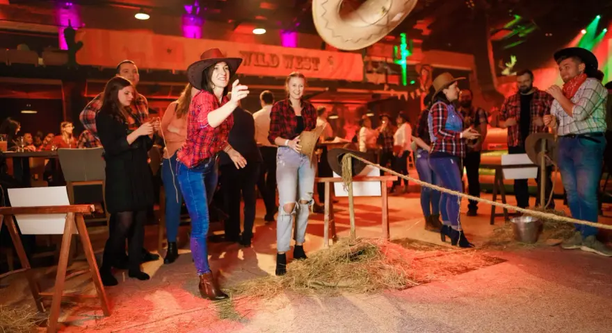 Impreza w stylu country: kobiety w kratkach i kapeluszach rzucają kapeluszem do celu.