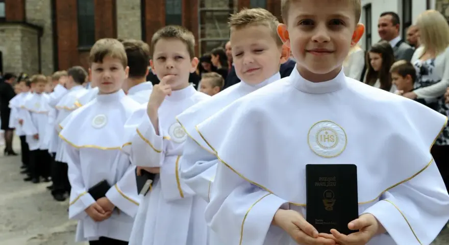 Chłopcy w białych albach, gotowi do komunii, trzymają modlitewniki. Jeden z nich uśmiecha się do aparatu.