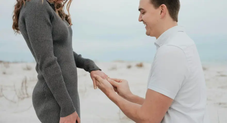 Mann macht Heiratsantrag am Strand. Ab wann darf man sich verloben? Das ist eine Frage der Liebe, nicht des Alters.