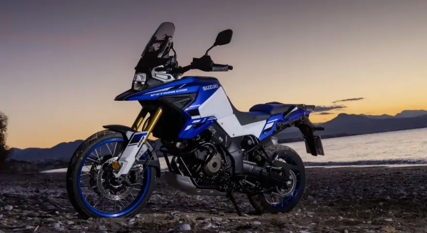 Suzuki V-Strom 1050 DE blu e bianca su una spiaggia al tramonto. Le opinioni su questa moto sono unanimi: avventura pura.