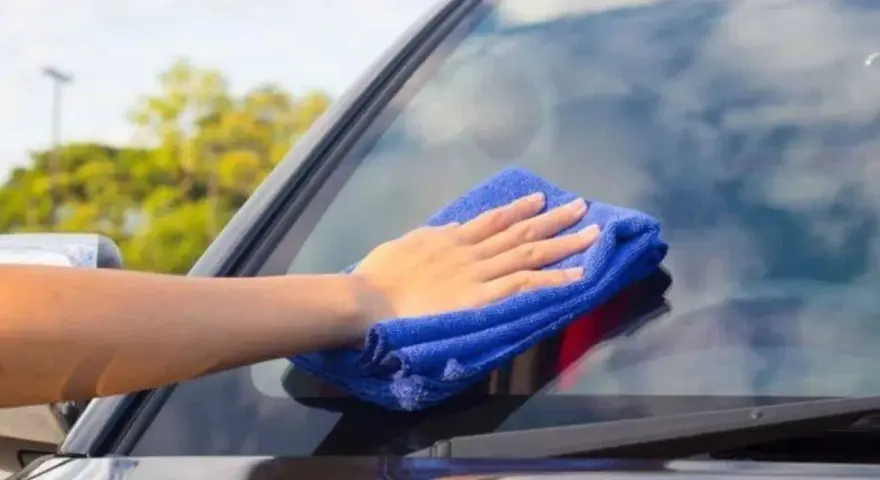 Mano con paño azul limpiando los cristales del coche para una visibilidad perfecta.
