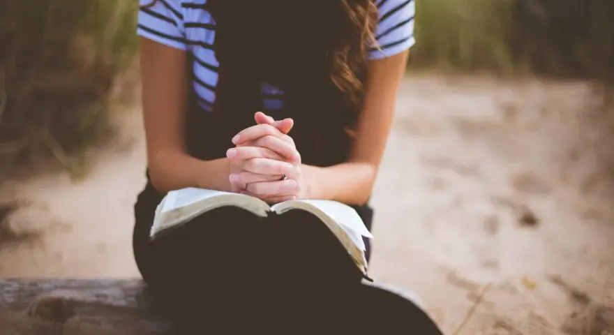 Frau mit verschränkten Händen über einem offenen Buch, die über ihre fertigen Gebete nachdenkt.