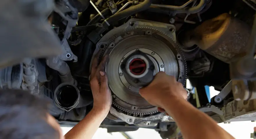 Mechanik dokonuje wymiany dwumasy w samochodzie, pracując przy skrzyni biegów.