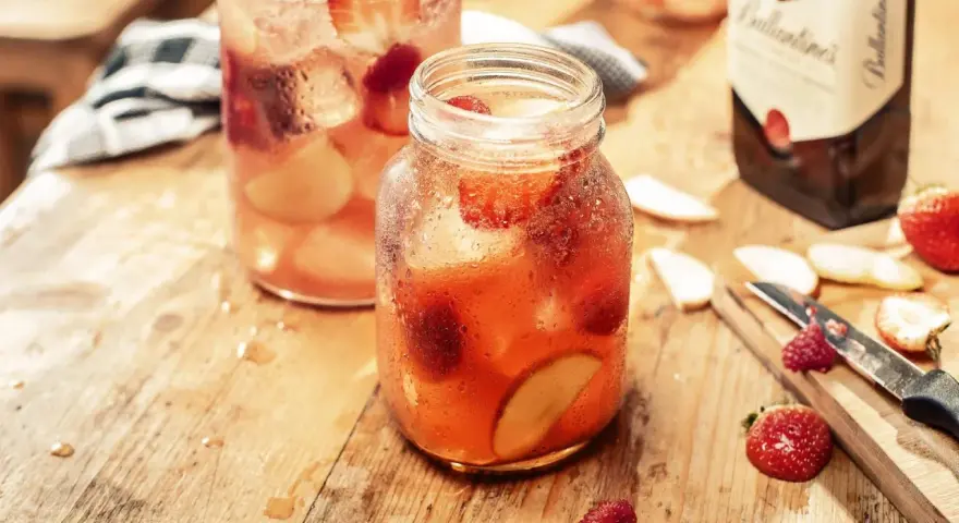 Orzeźwiający, kobiecy drink z whisky, pełen truskawek i jabłek, na drewnianym blacie.