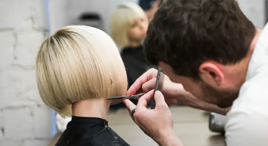 Fryzjerka tworzy modne fryzury odmładzające po 40 krótkie. Blond bob jest precyzyjnie cięty.