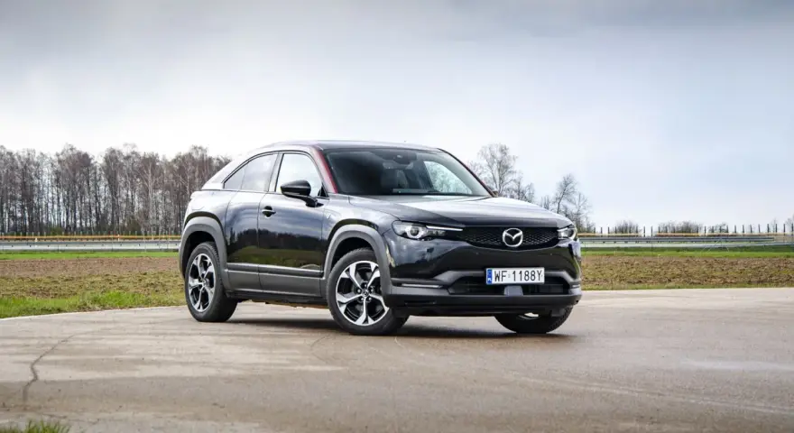 Czarna Mazda MX-30 na tle pochmurnego nieba i drzew.