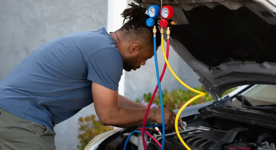 Man working on car engine, using gauges and hoses to fix car AC.