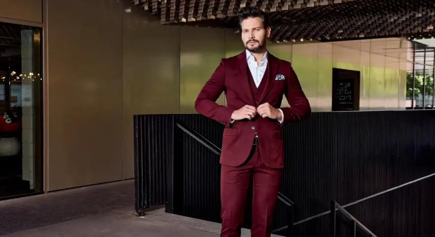 Elegancki mężczyzna w bordowym garniturze i marynarce zapina guziki.