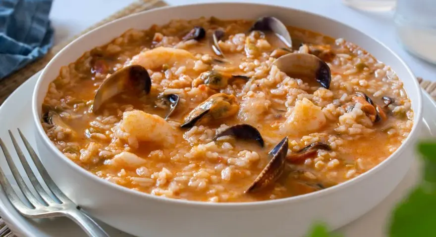Un delicioso arroz caldoso de marisco, repleto de gambas, mejillones y almejas, servido en un cuenco blanco.
