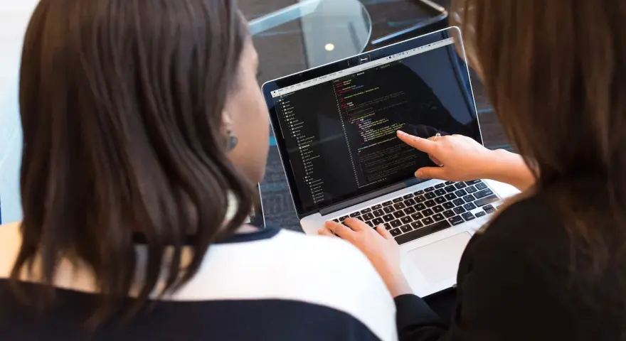Due persone analizzano codice su un laptop. Una indica una riga, mostrando cosa fa un analista funzionale.