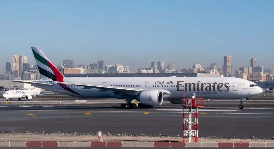 Samolot Emirates na płycie lotniska, w tle panorama Dubaju. Zastanawiasz się, ile się leci do Dubaju?