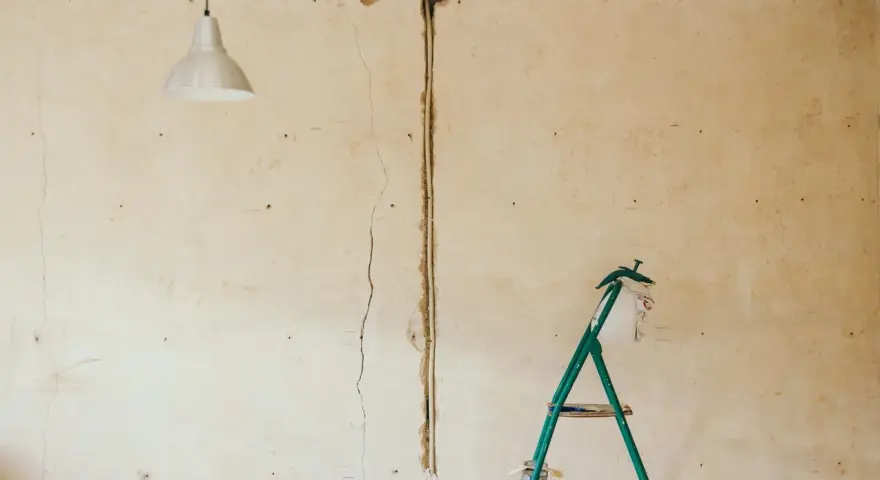 Pękające ściany starego domu, widoczna instalacja elektryczna i drabina.