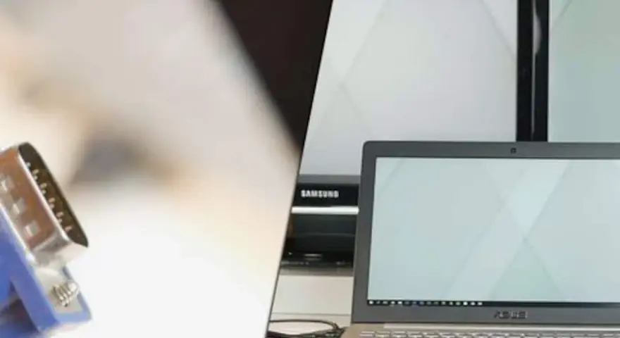 Ein VGA-Kabel wird verwendet, um einen Laptop mit einem Bildschirm zu verbinden. Mehrere Monitore sind im Hintergrund zu sehen.