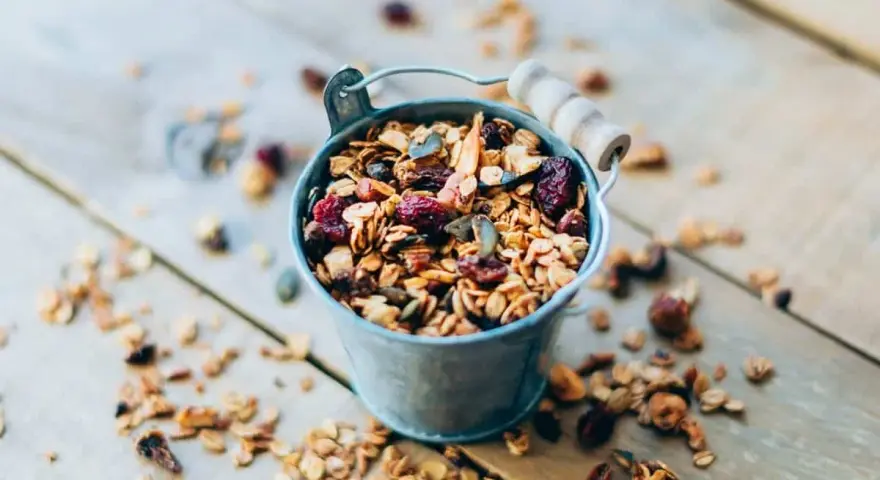 Un cubo metálico lleno de granola casera, con arándanos y semillas. ¡Perfecto para saber como hacer granola!