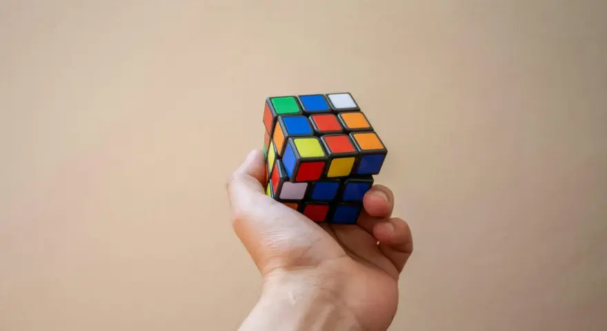 En hand håller en färgglad rubiks kub nyckelring mot en ljus bakgrund.