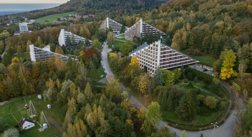 Widok z lotu ptaka na sanatoria o trójkątnej architekturze w otoczeniu jesiennego lasu.
