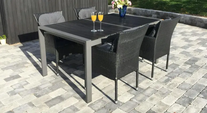 En uteplats med stenläggning, ett mörkt bord med korgstolar och glas med juice.