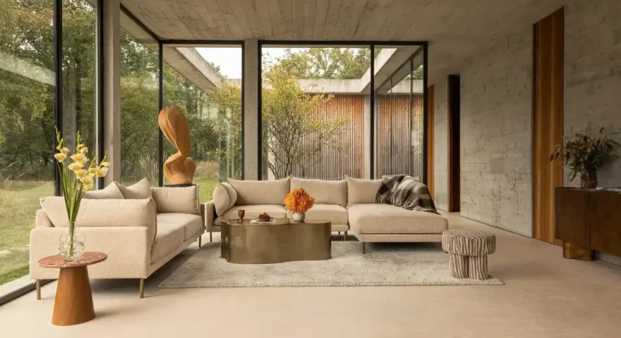 Sofá seccional beige y sillón en un salón moderno con grandes ventanales. Las combinaciones con beige crean un ambiente sereno y elegante.