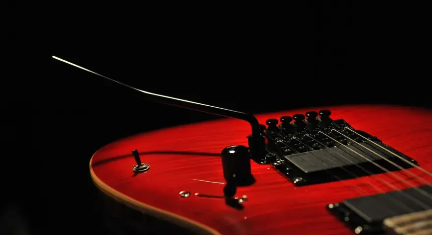 Czerwona gitara elektryczna z czarnym mostkiem tremolo, gotowa do wydobycia dźwięków, które poruszą serce.