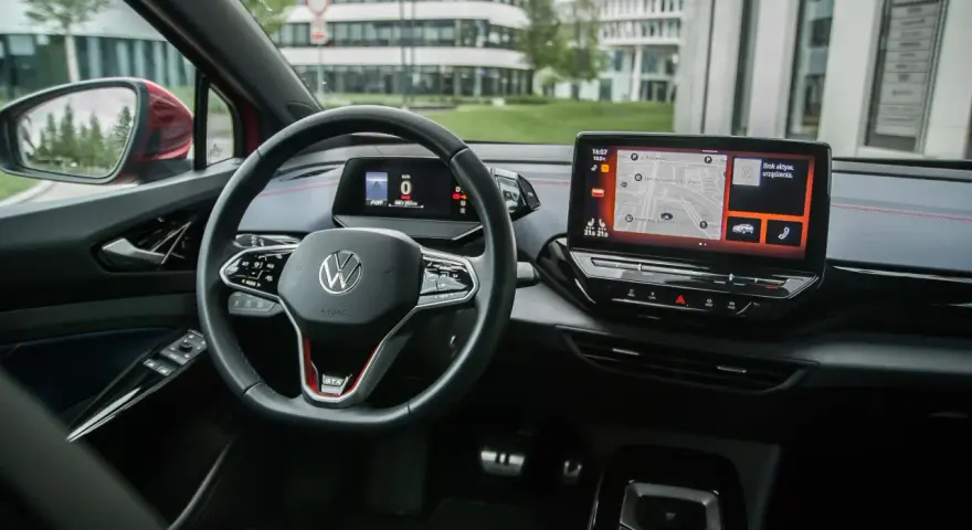 Wnętrze Volkswagena ID.4 GTX z ekranem nawigacji i cyfrowym kokpitem. Kierownica z przyciskami i oznaczeniem GTX.
