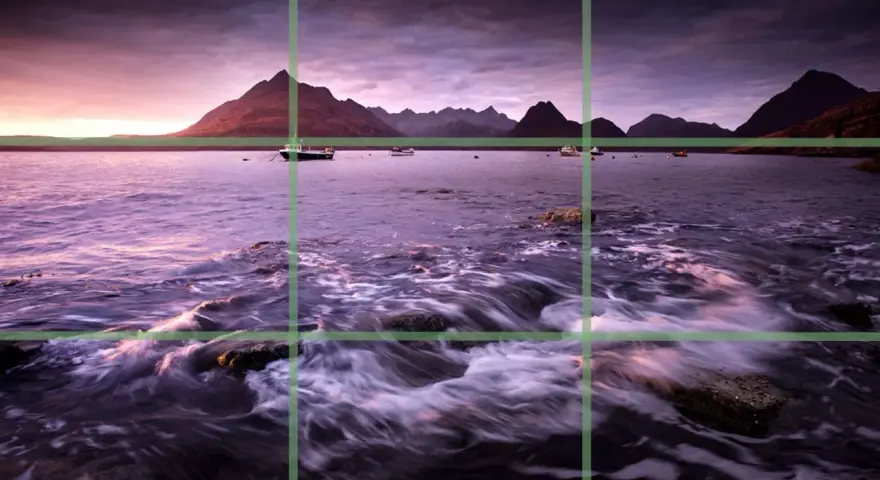 Paysage marin au crépuscule, avec des montagnes en arrière-plan et des bateaux sur l'eau. La composition suit la règle des tiers pour un équilibre visuel.