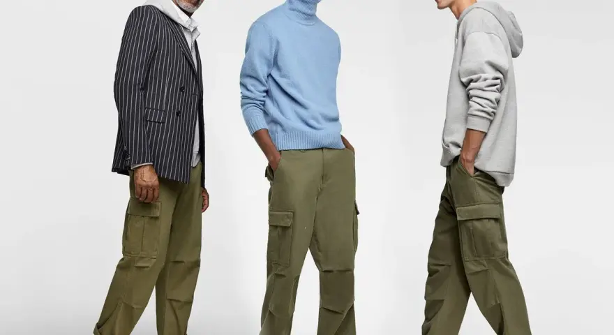 Tres hombres posan con pantalones cargo y camisas. Uno lleva un blazer a rayas, otro un suéter azul y el tercero una sudadera gris.